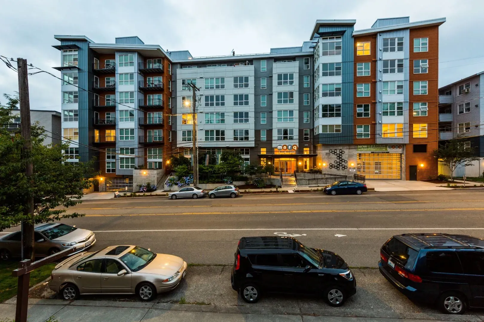 Exterior view of the modern apartment building with a street and parked cars in the foreground.