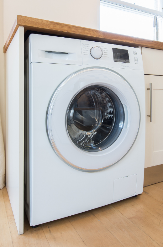 A white washing machine is sitting on top of a wooden counter in a kitchen.