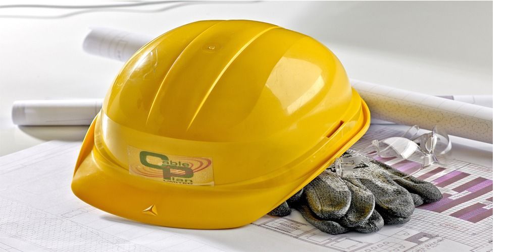 A yellow hard hat and work gloves resting on a set of architectural blueprints.
