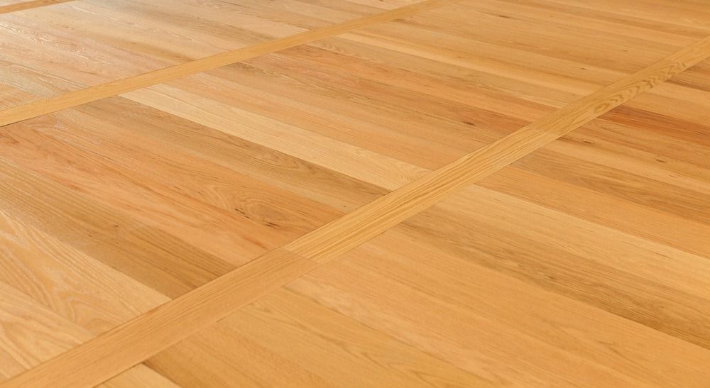 A close-up view of light-colored, natural wood flooring with a distinct geometric panel pattern.