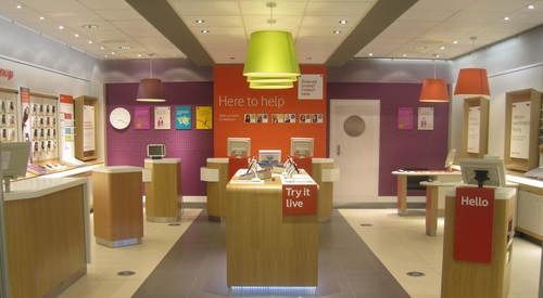 A retail store interior with wood-paneled service counters, orange and purple walls, and large overhead light fixtures.