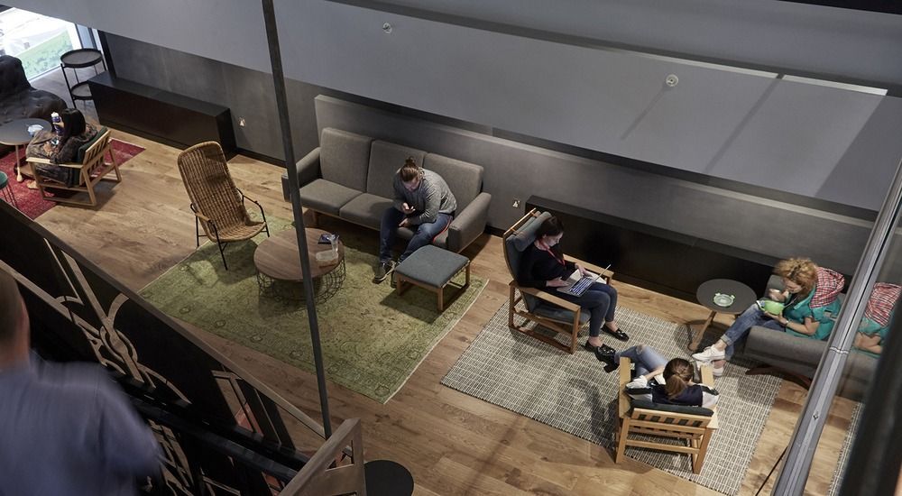 High-angle view of a modern lounge area with people seated on sofas and chairs on rugs over a hardwood floor.