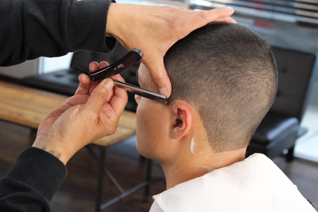 A man is getting his hair cut by a barber with a razor.