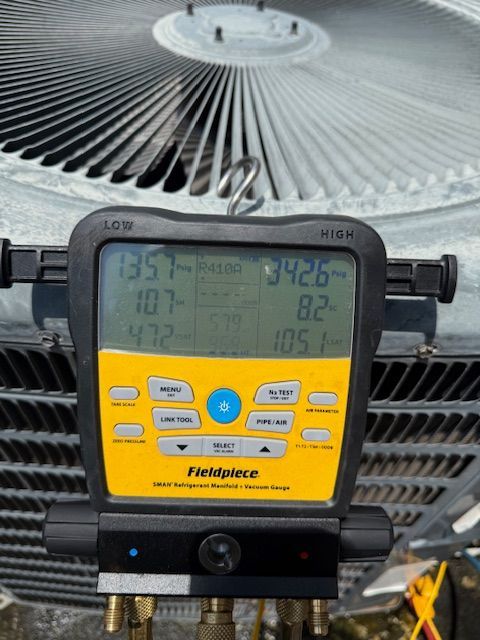 Person checks air conditioning unit with gauges and hoses.