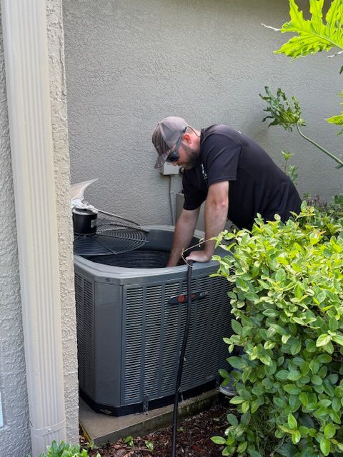 Man removing air vent cover from the ceiling. He wears a yellow shirt and looks upward.