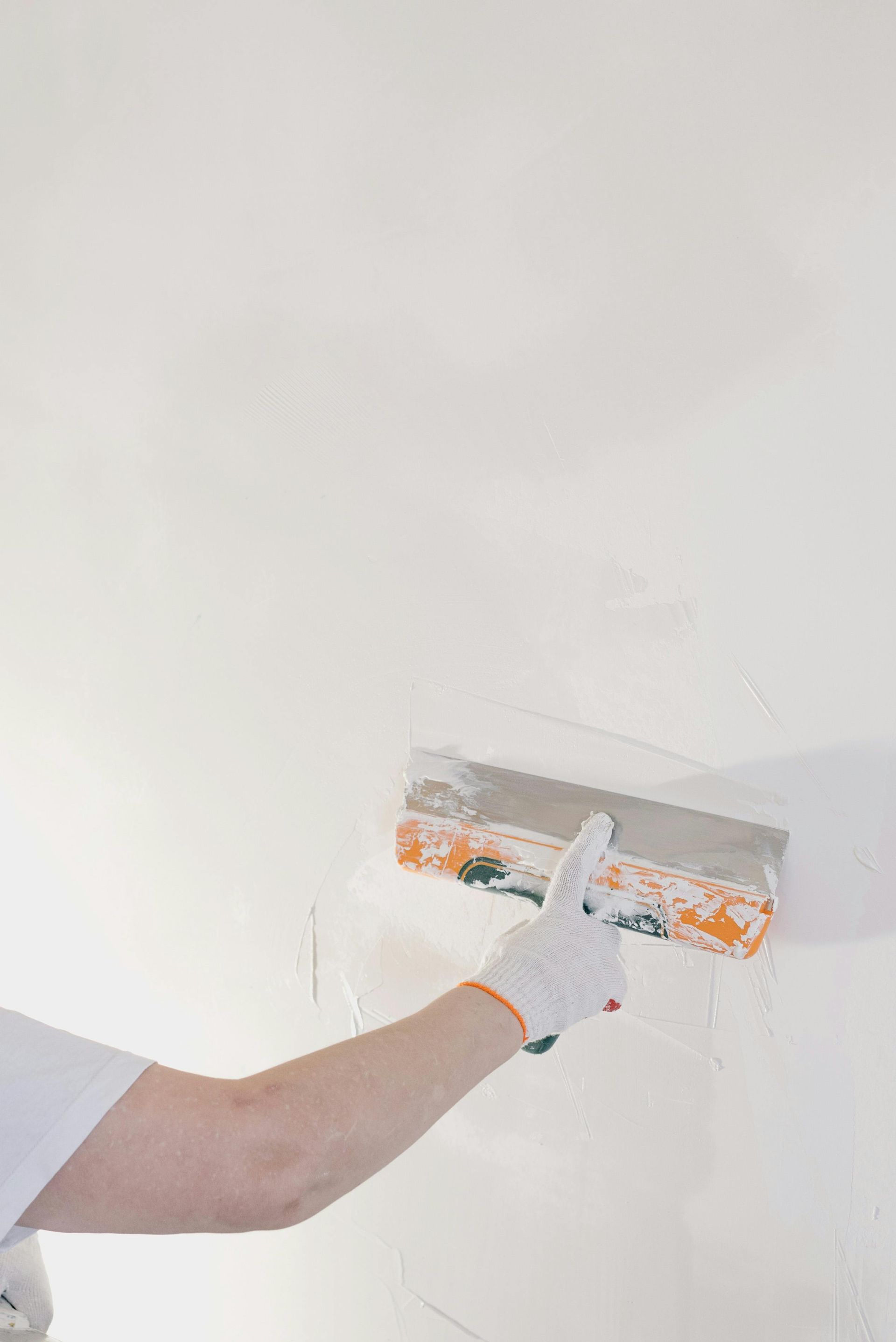 Person wearing a glove, uses a trowel to apply white compound to a white wall.