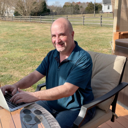 A man in a blue shirt is typing on a laptop
