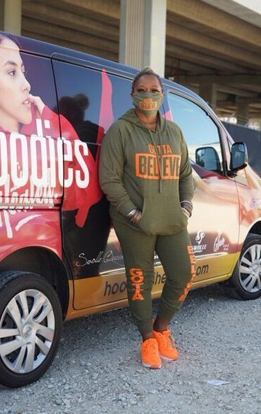 A woman wearing a mask is standing in front of a van that says hoodies