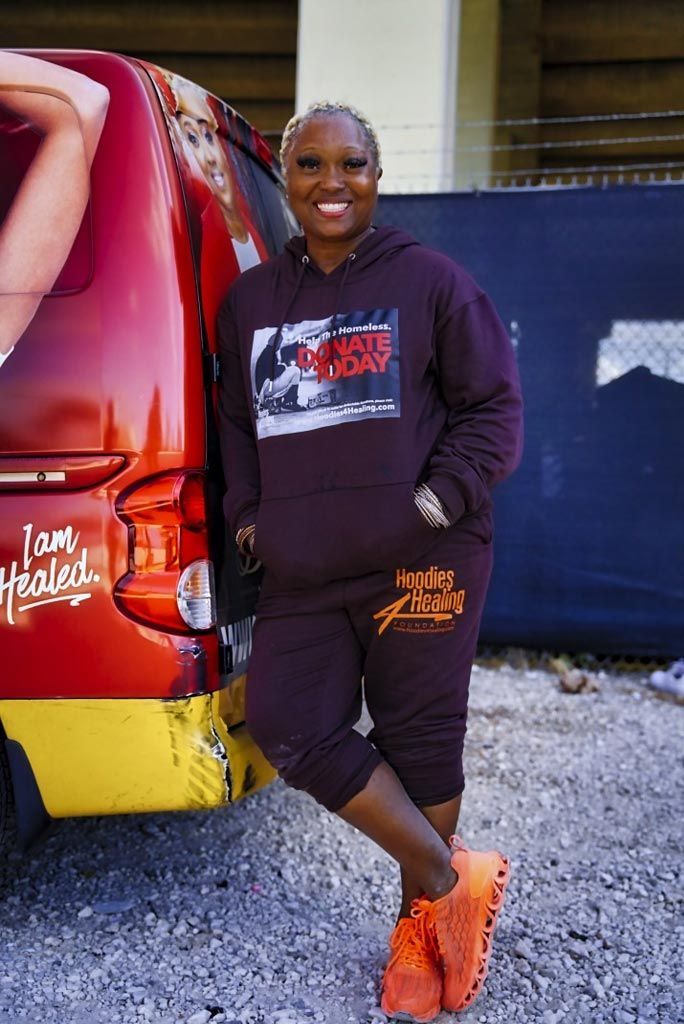 A woman in a maroon hoodie is standing in front of a red van.