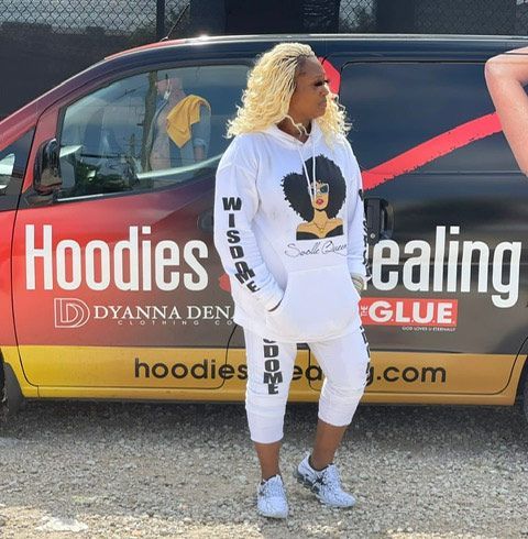 A woman is standing in front of a van that says hoodies healing glue