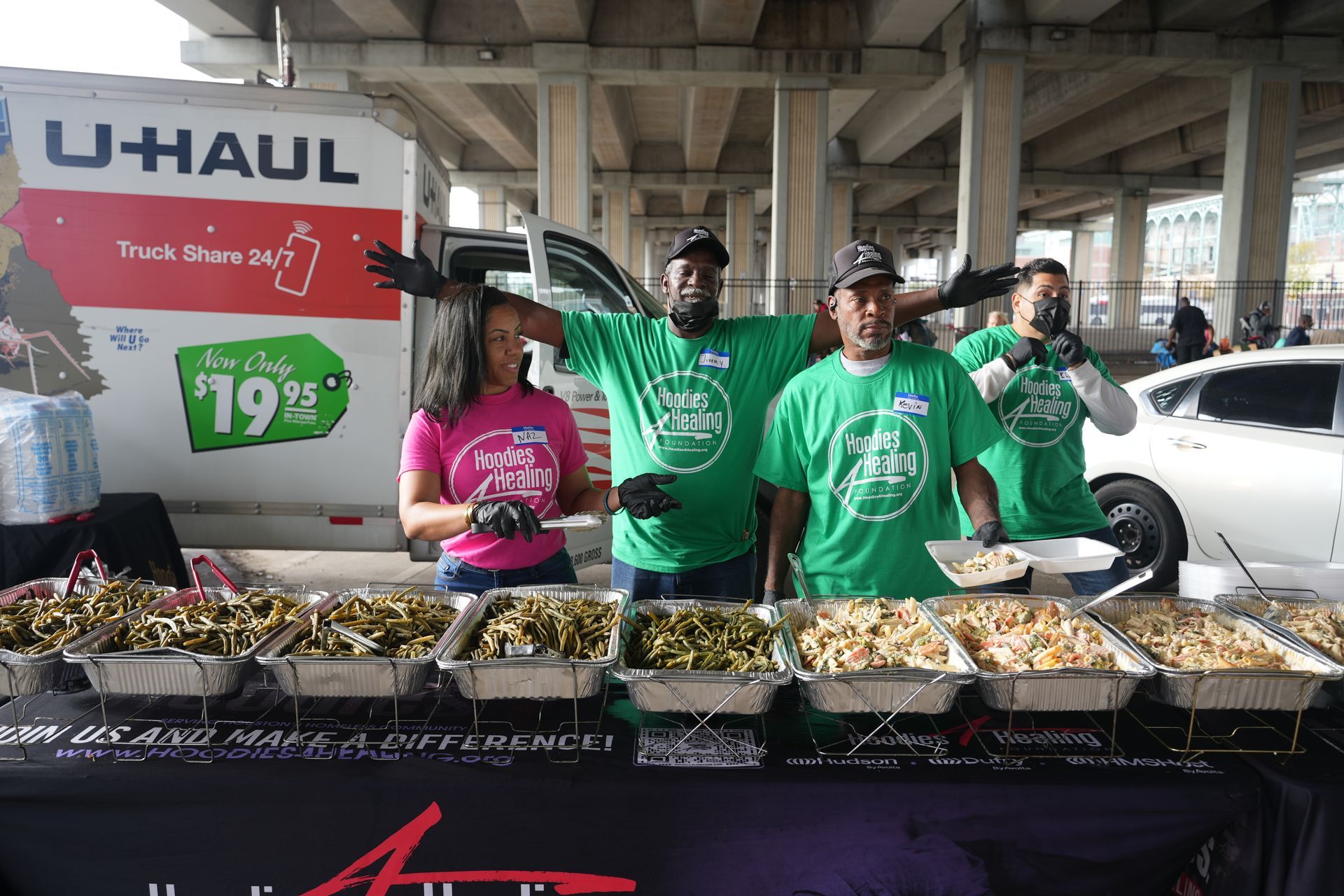 A group of people standing in front of a uhaul truck serving food.