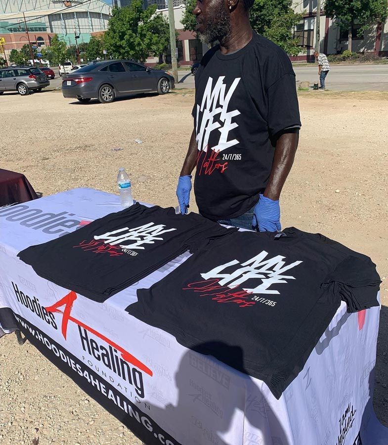 A man standing next to a table with t-shirts on it that say my life