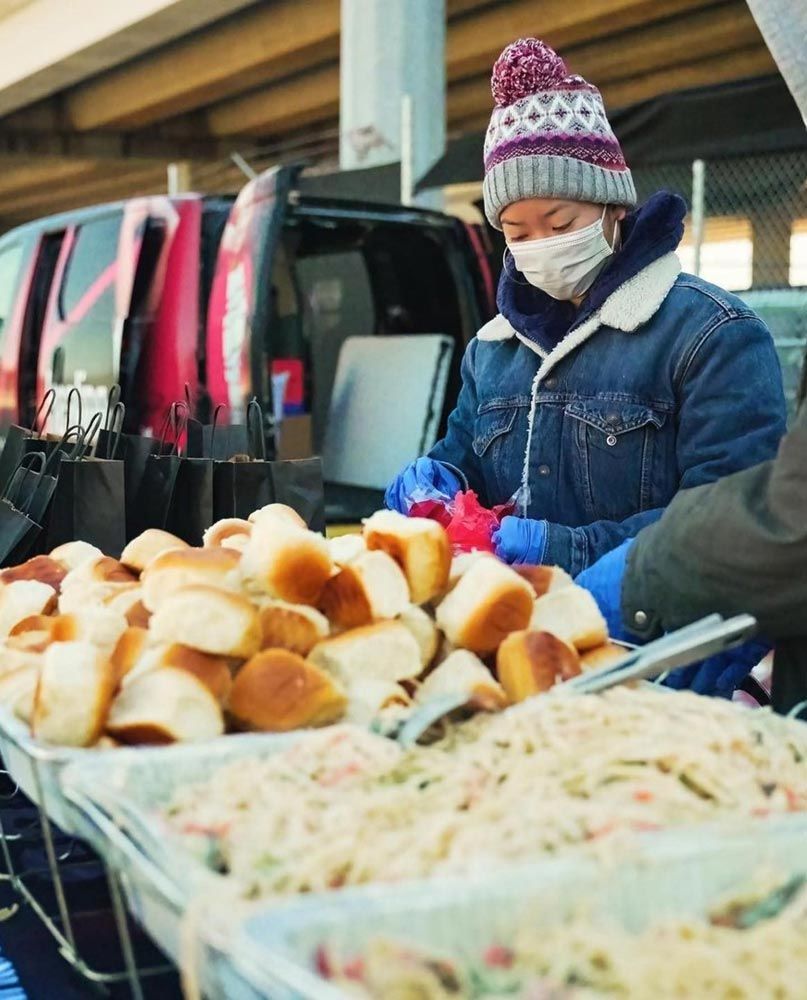 A woman wearing a mask is standing in front of a table full of food.
