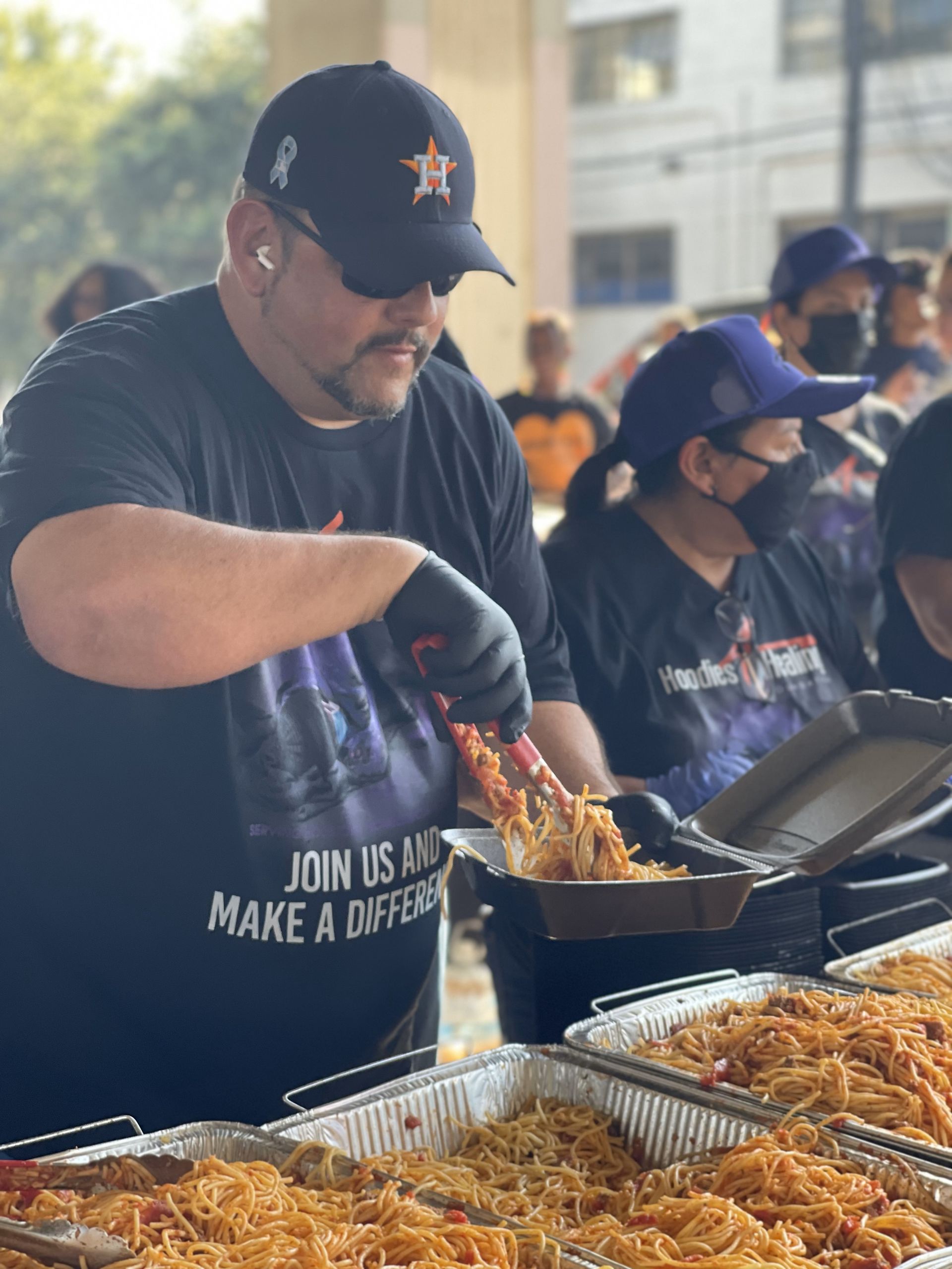 A man wearing a black shirt that says join us to make a difference is preparing food.