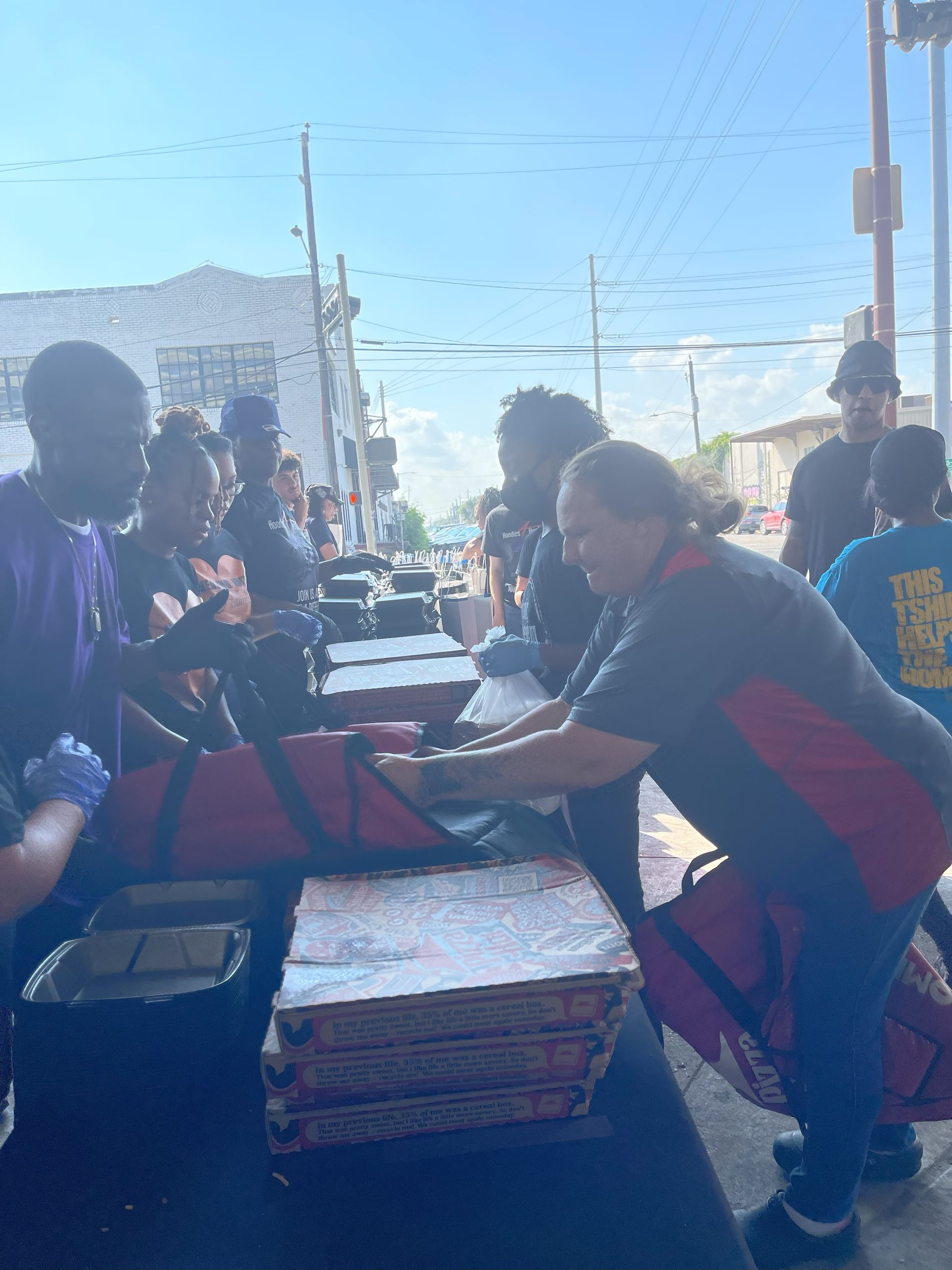 A group of people are gathered around a stack of pizza boxes.