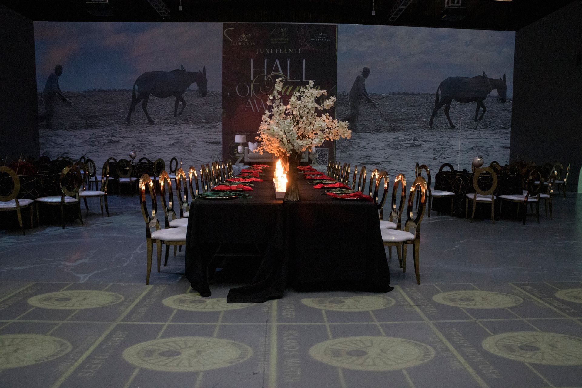 A long table with a vase of flowers on it in front of a wall with horses on it.