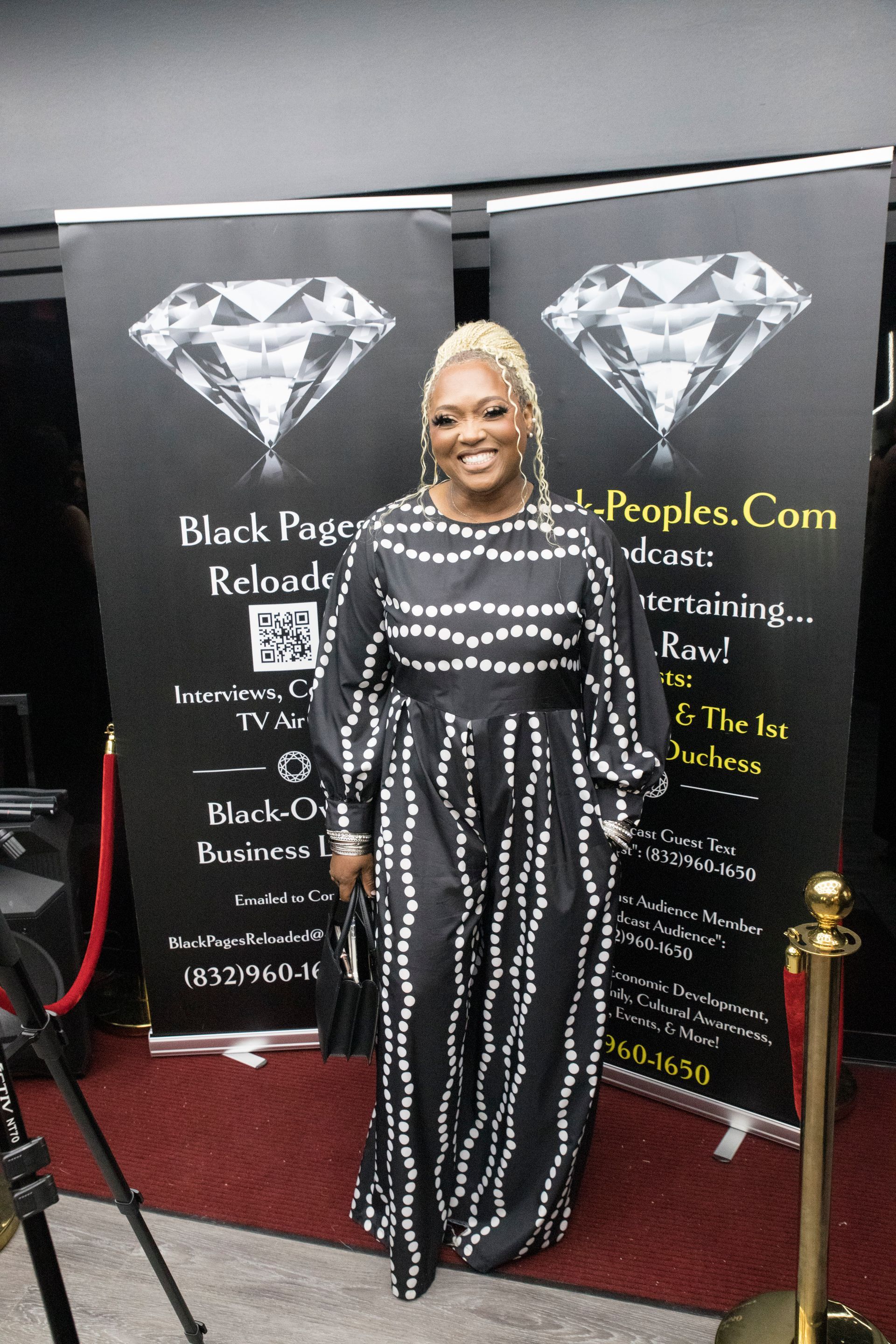 A woman in a black and white dress is standing in front of a black banner with a diamond on it.
