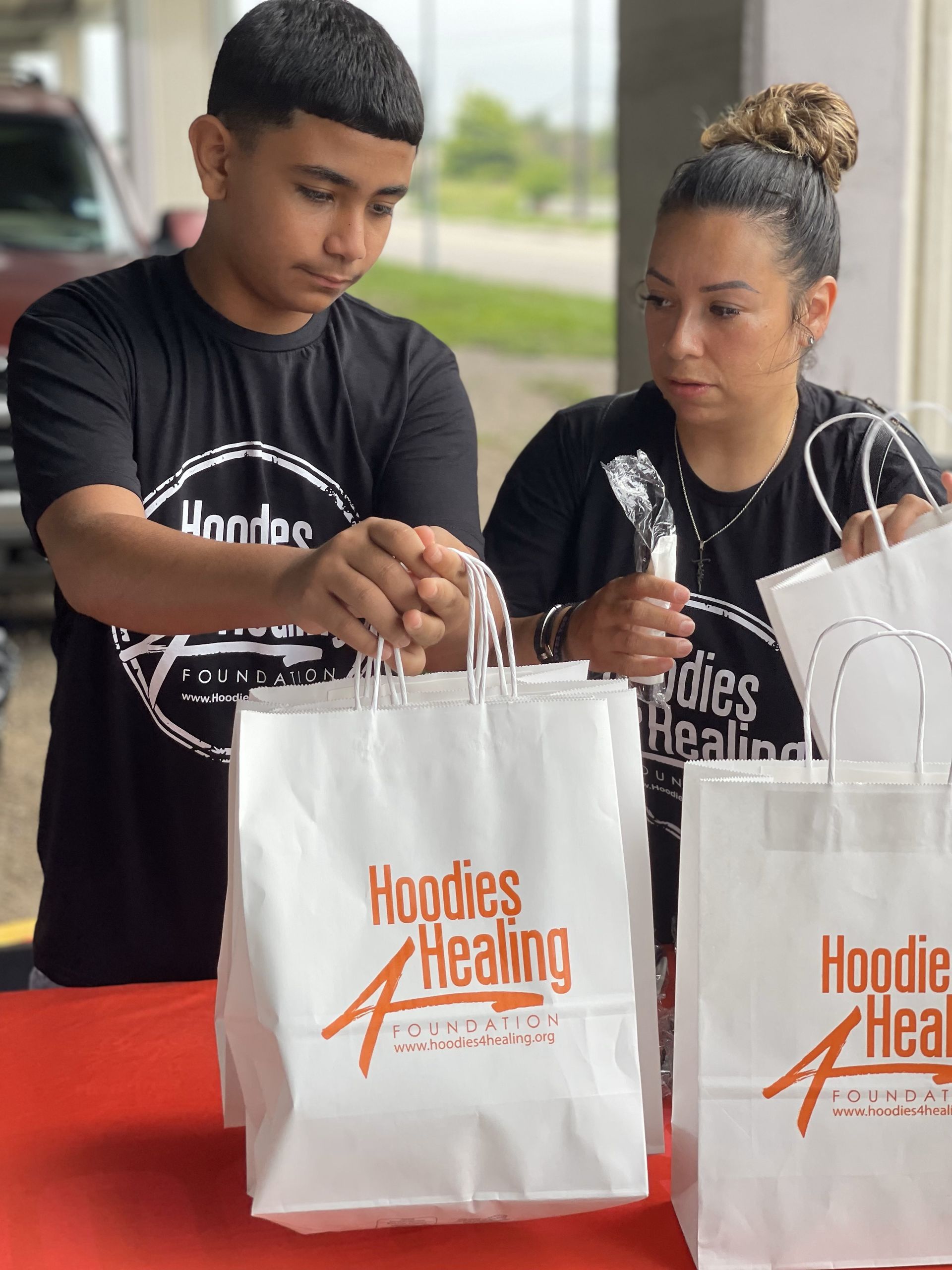 A man and a woman are holding bags that say hoodies healing on them.