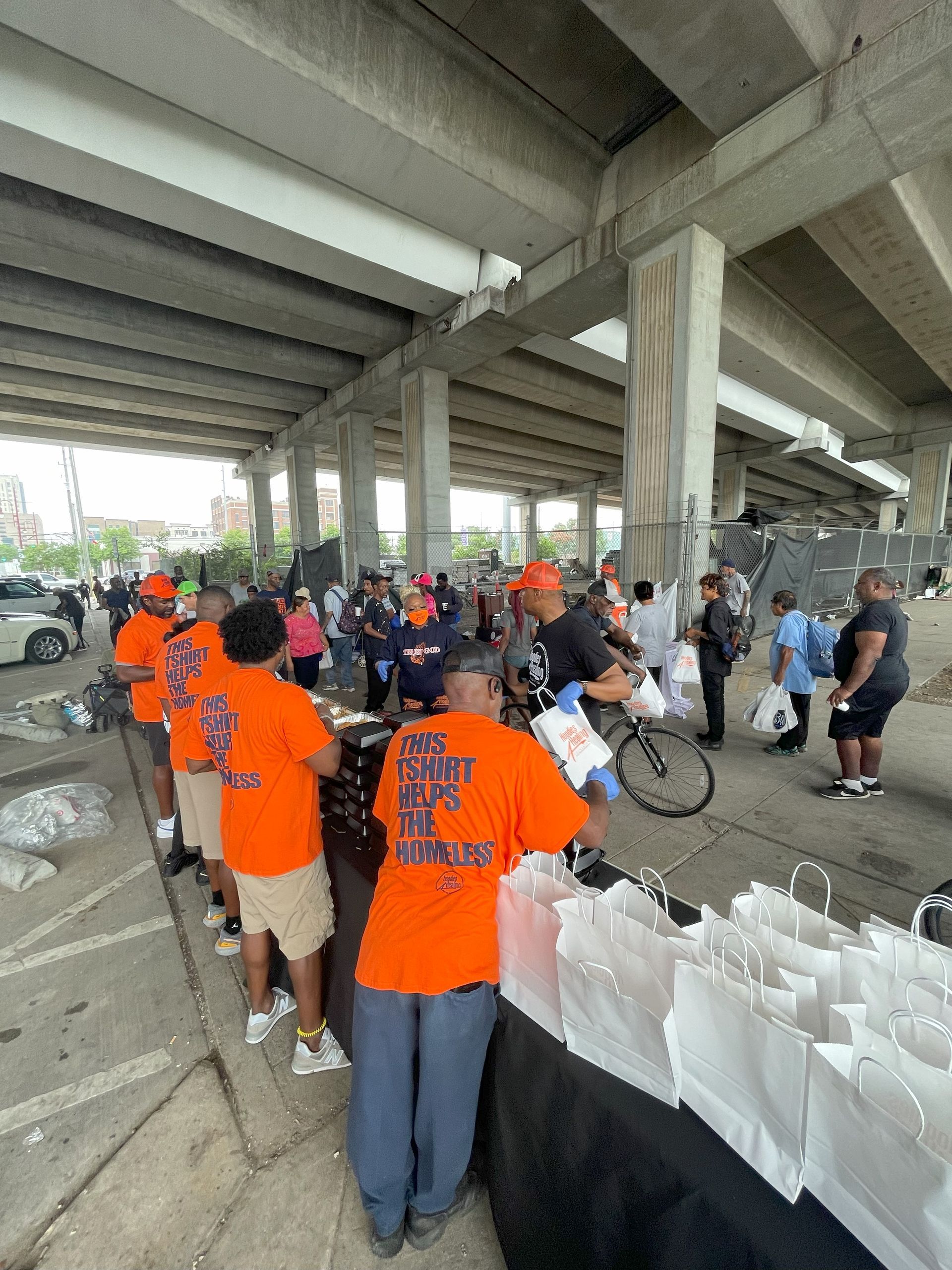 A group of people are standing in a parking lot under a bridge.