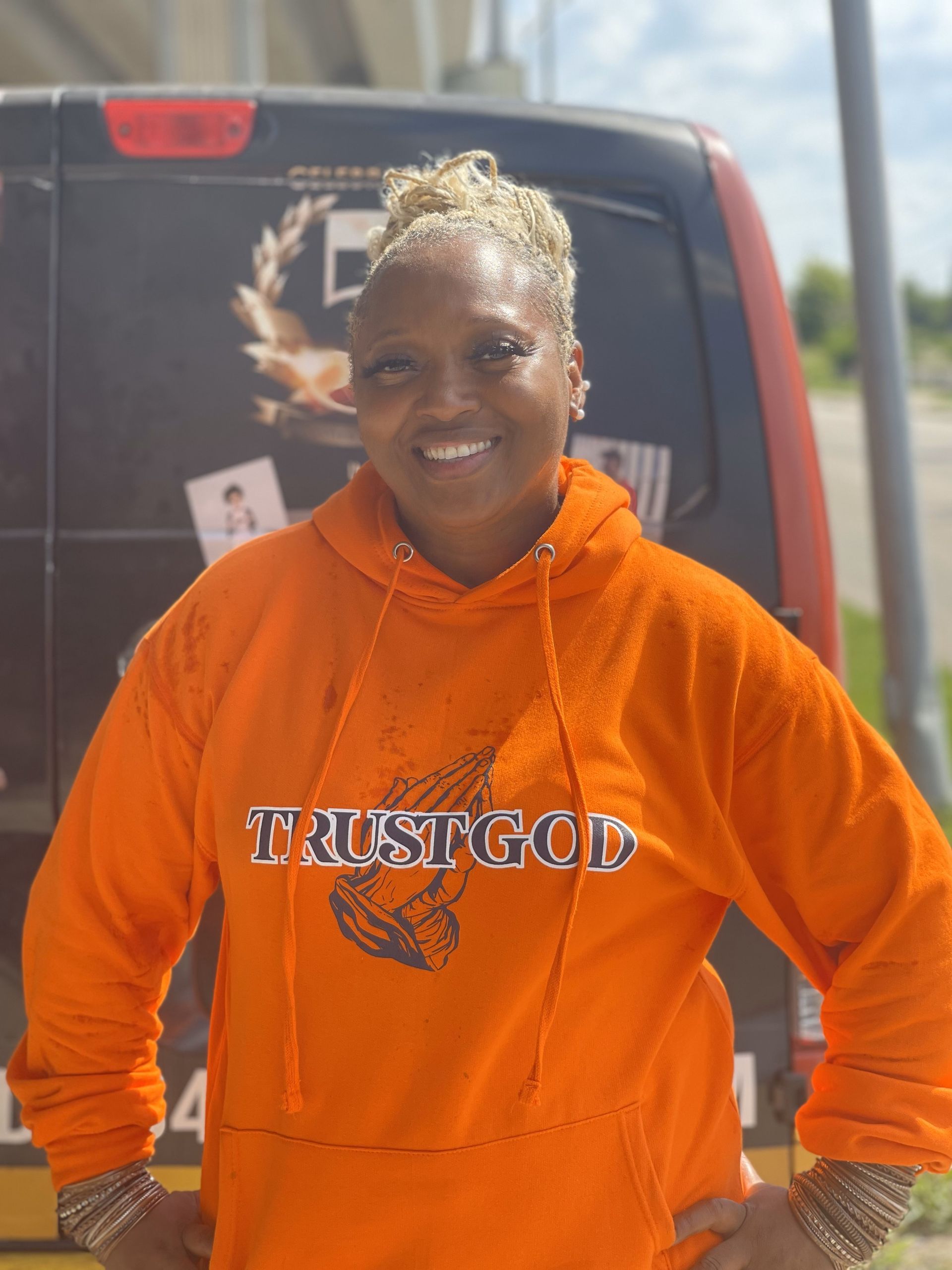 A woman wearing an orange hoodie is standing in front of a van.