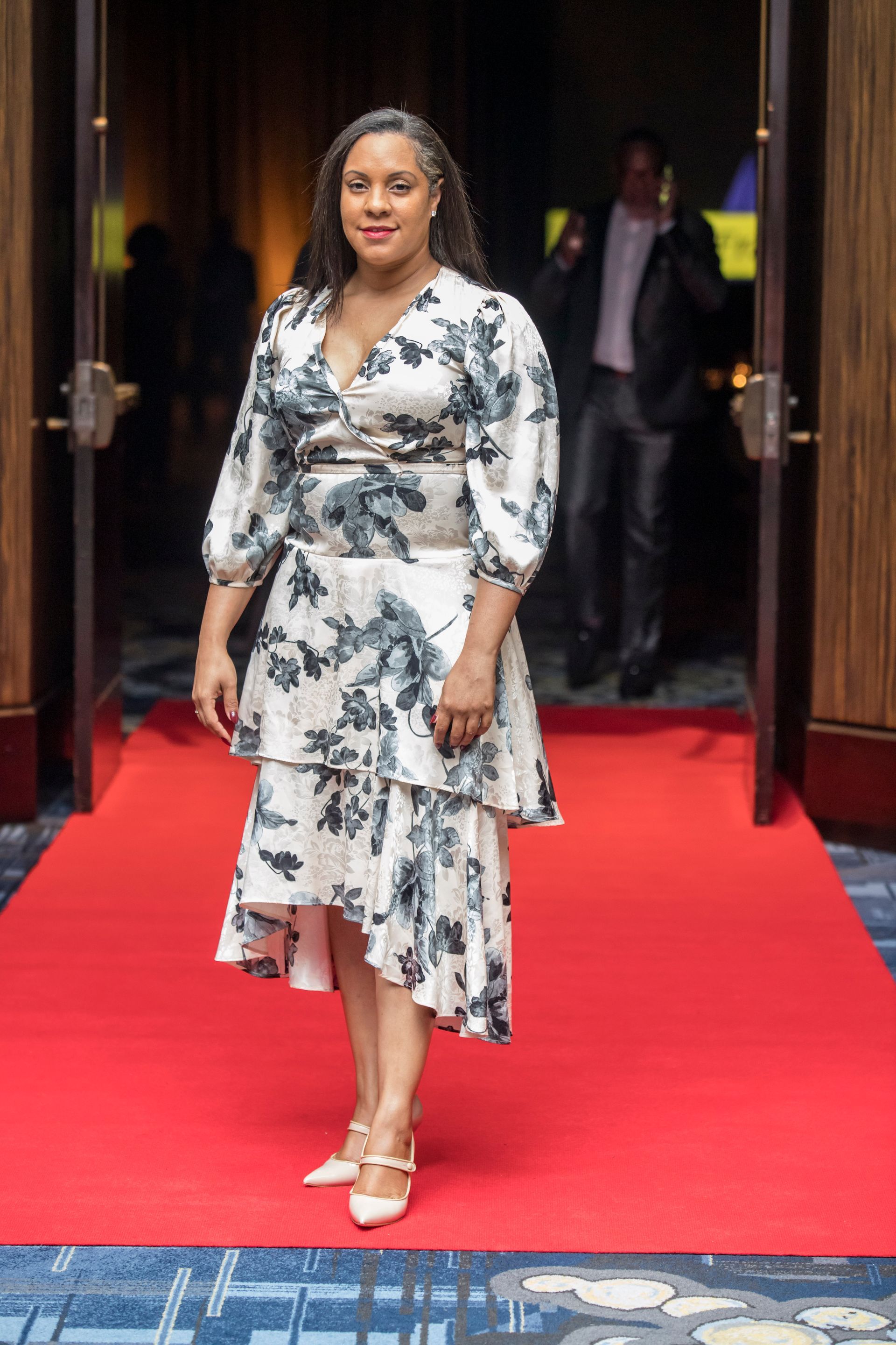 A woman in a floral dress is standing on a red carpet.