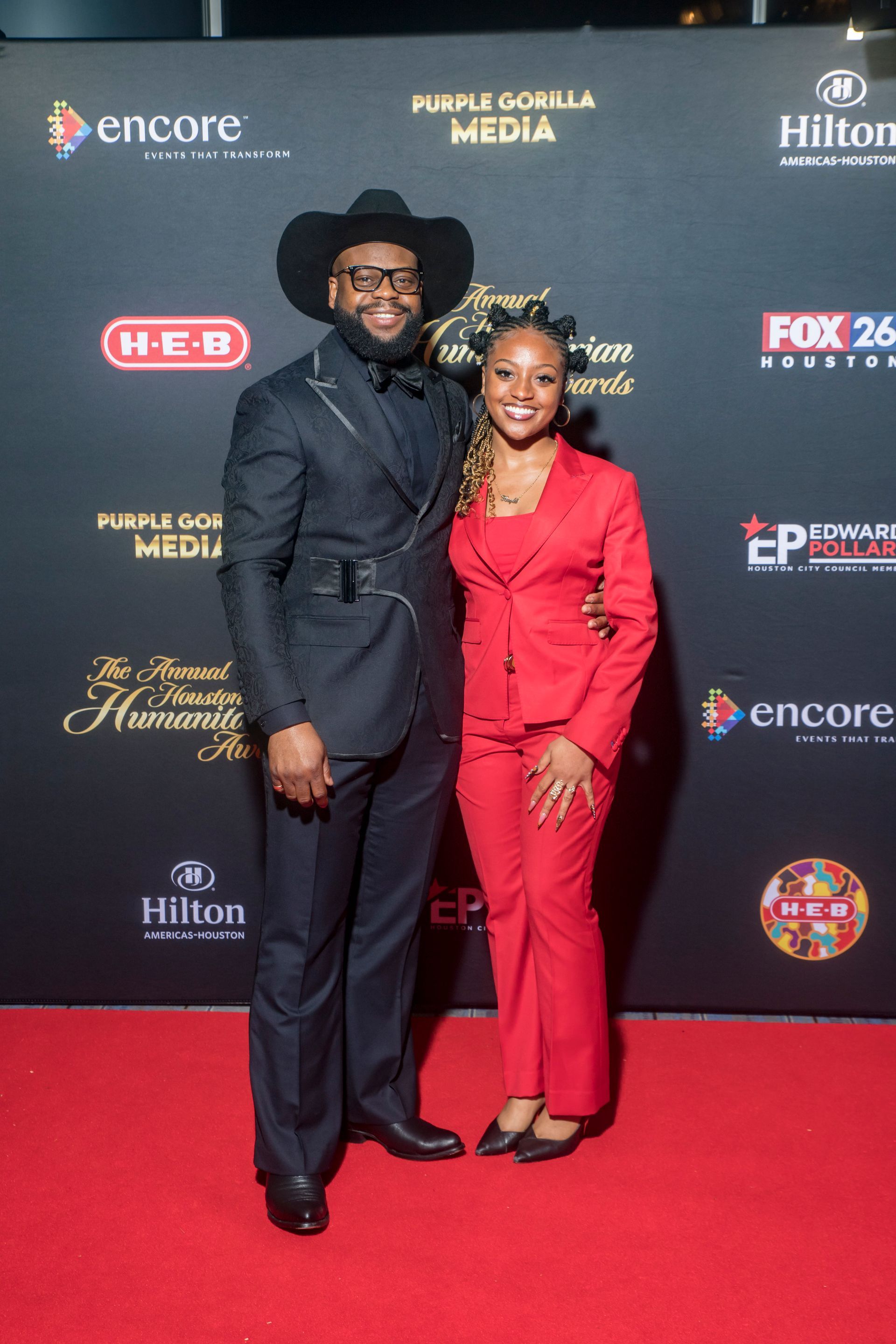 A man and a woman are posing for a picture on a red carpet.