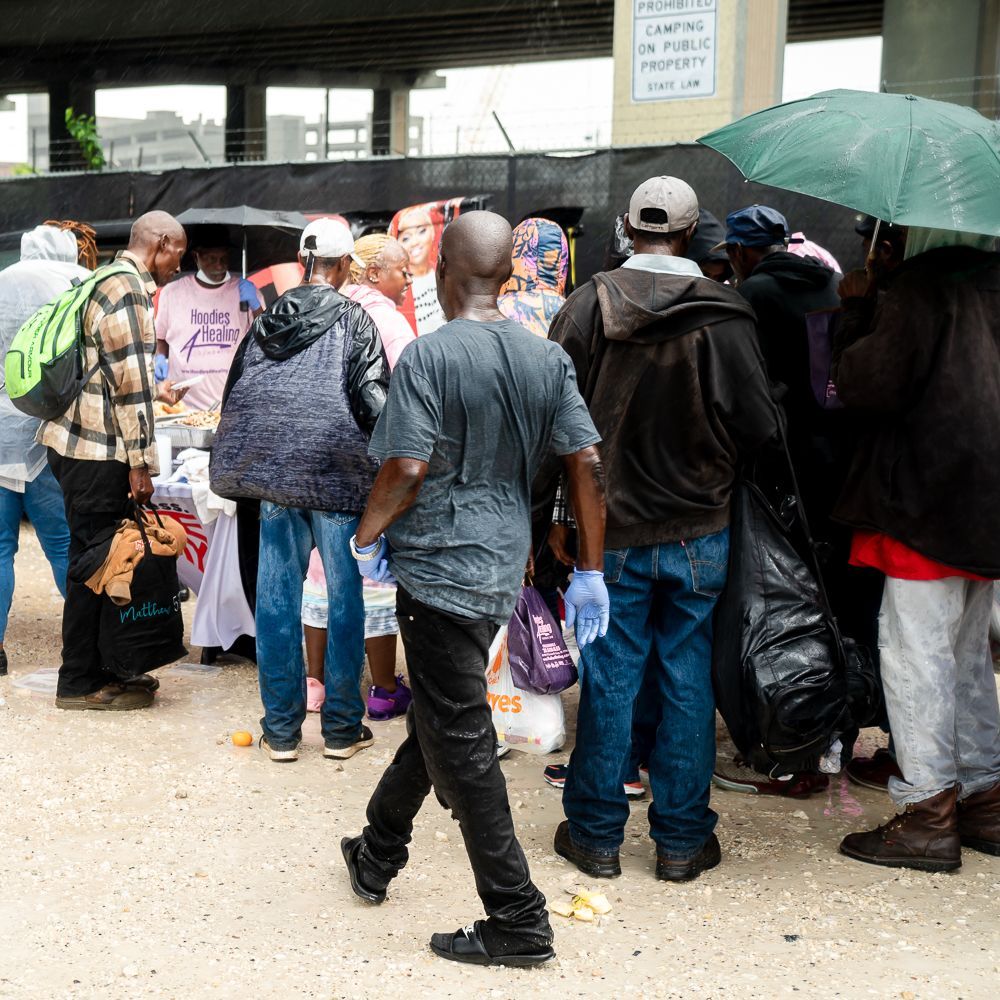 A group of people are gathered under an umbrella in front of a sign that says no parking on public property