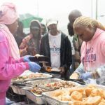 A group of people are standing around a table filled with food.