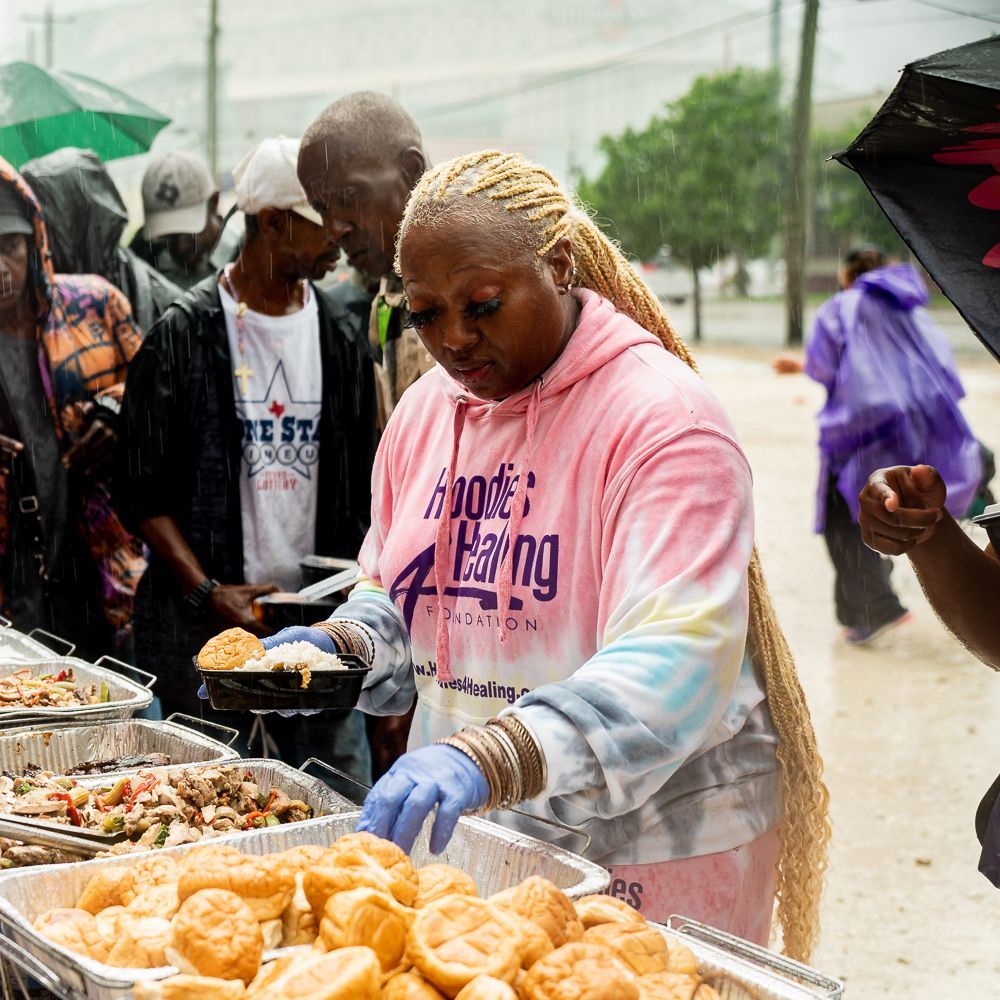 A woman in a pink hoodie is serving food to a group of people.