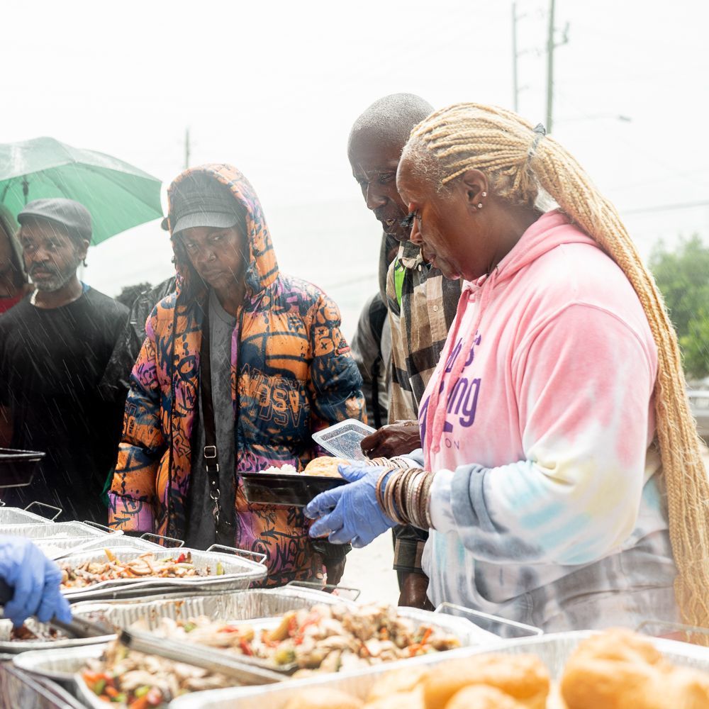 A woman in a pink hoodie is serving food to a group of people