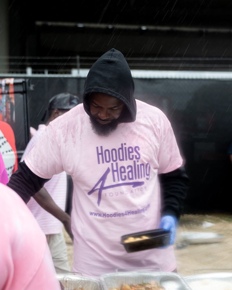 A man wearing a pink shirt that says hoodies healing