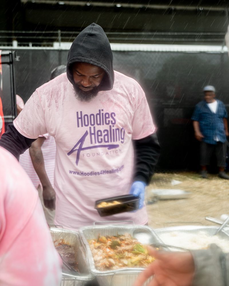 A man wearing a pink shirt that says hoodies healing
