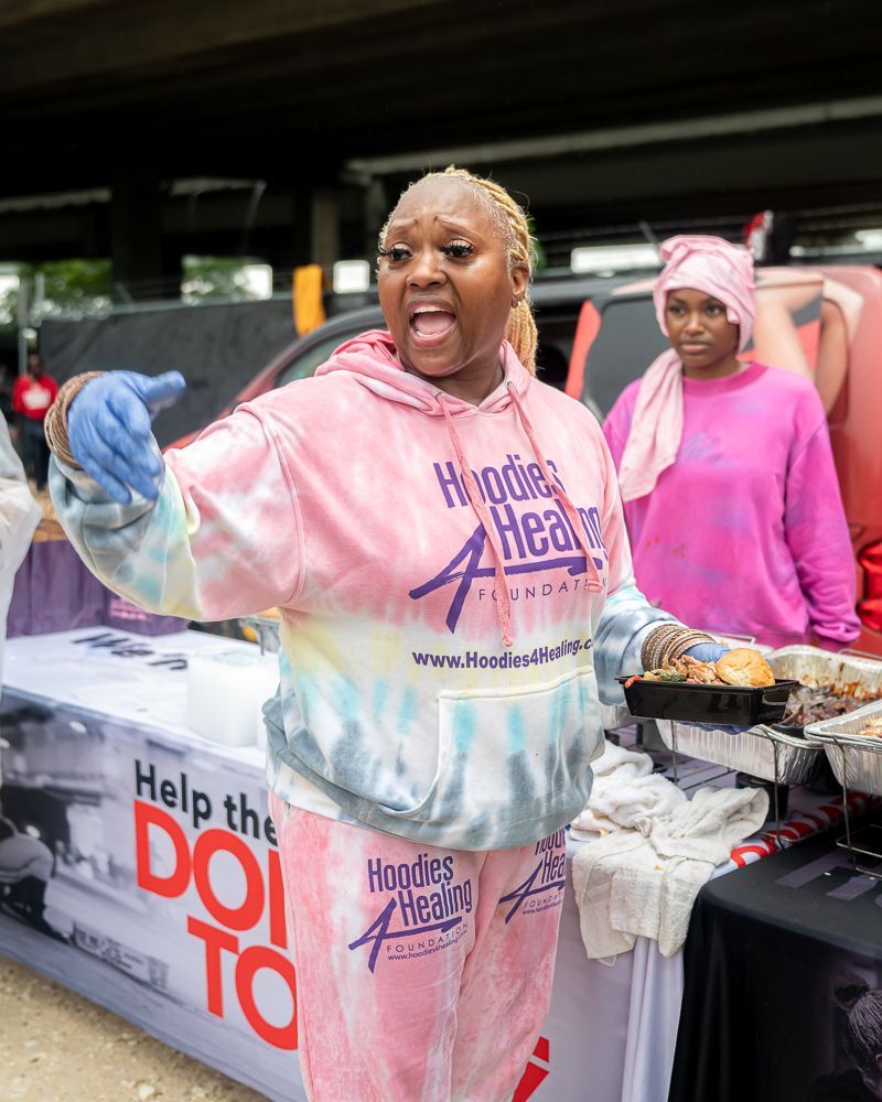A woman in a tie dye hoodie is standing in front of a table holding a tray of food.