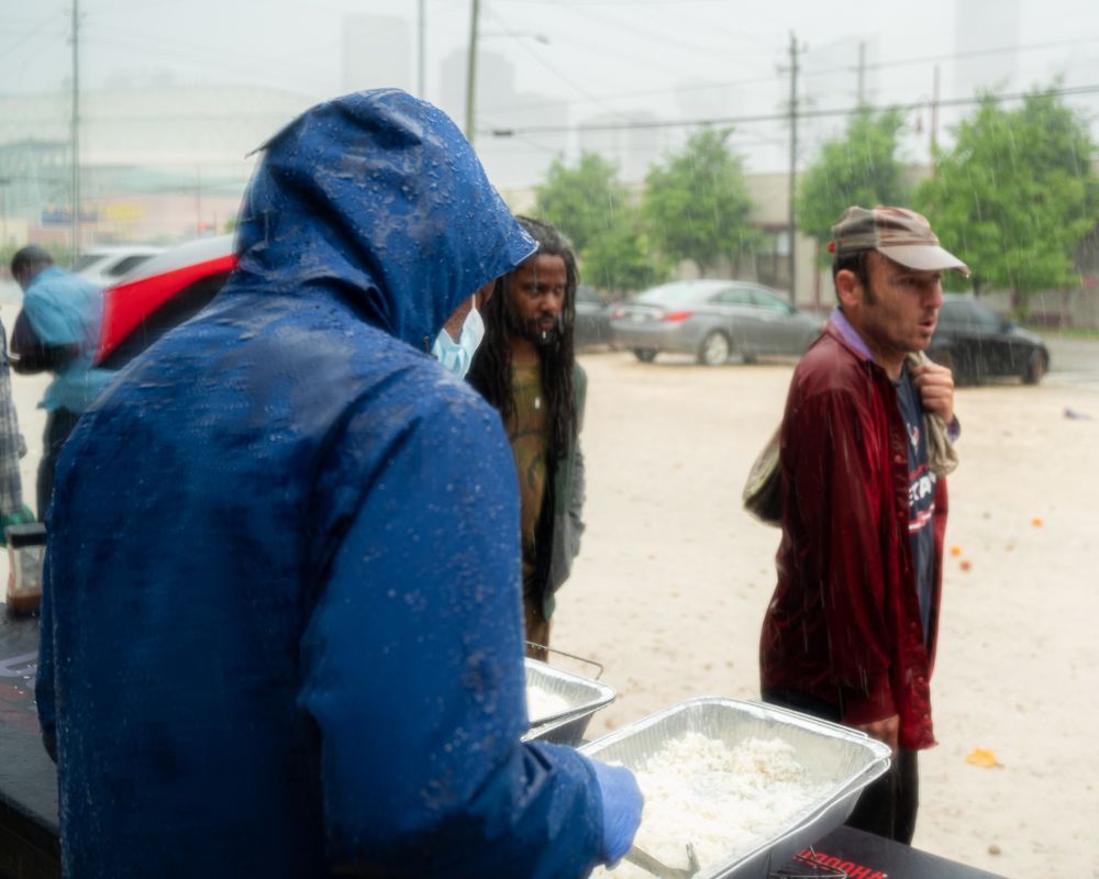 A man in a blue raincoat is standing in front of a table with a tray of food.
