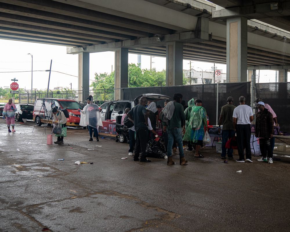 A group of people are standing in a parking lot under a bridge