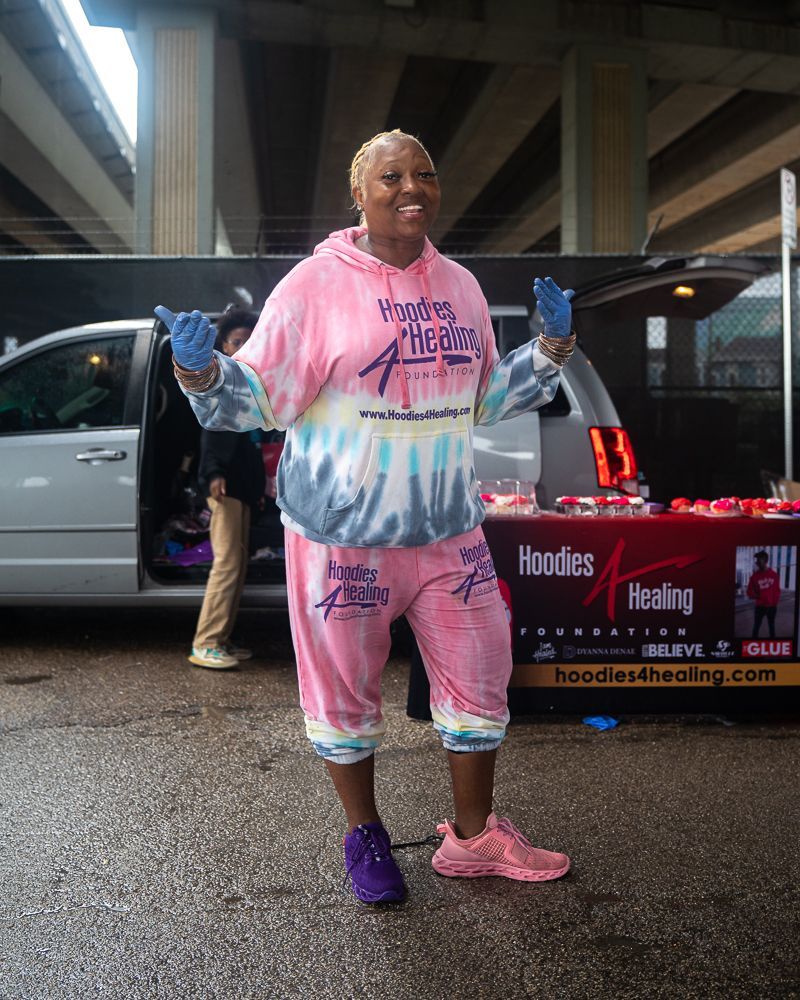 A woman in a pink tie dye hoodie is standing in front of a van.
