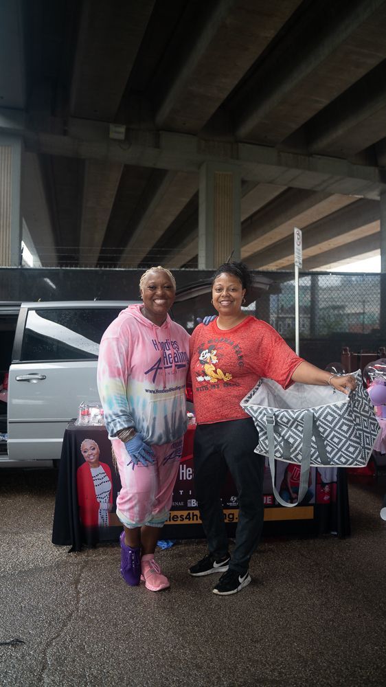 Two women are standing next to each other under a bridge holding a bag.