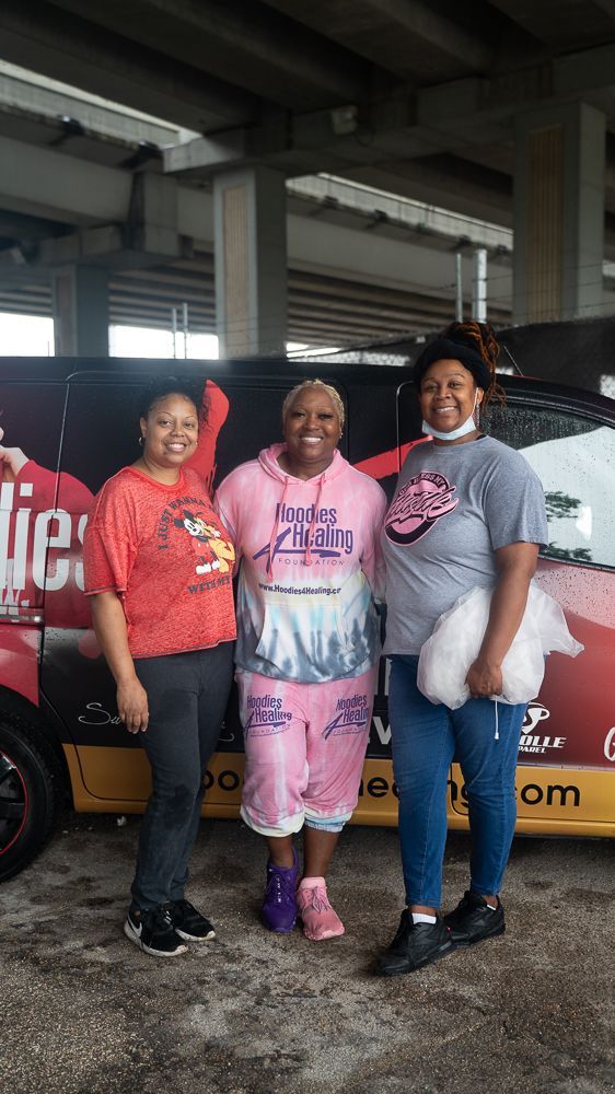 Three women are posing for a picture in front of a van.
