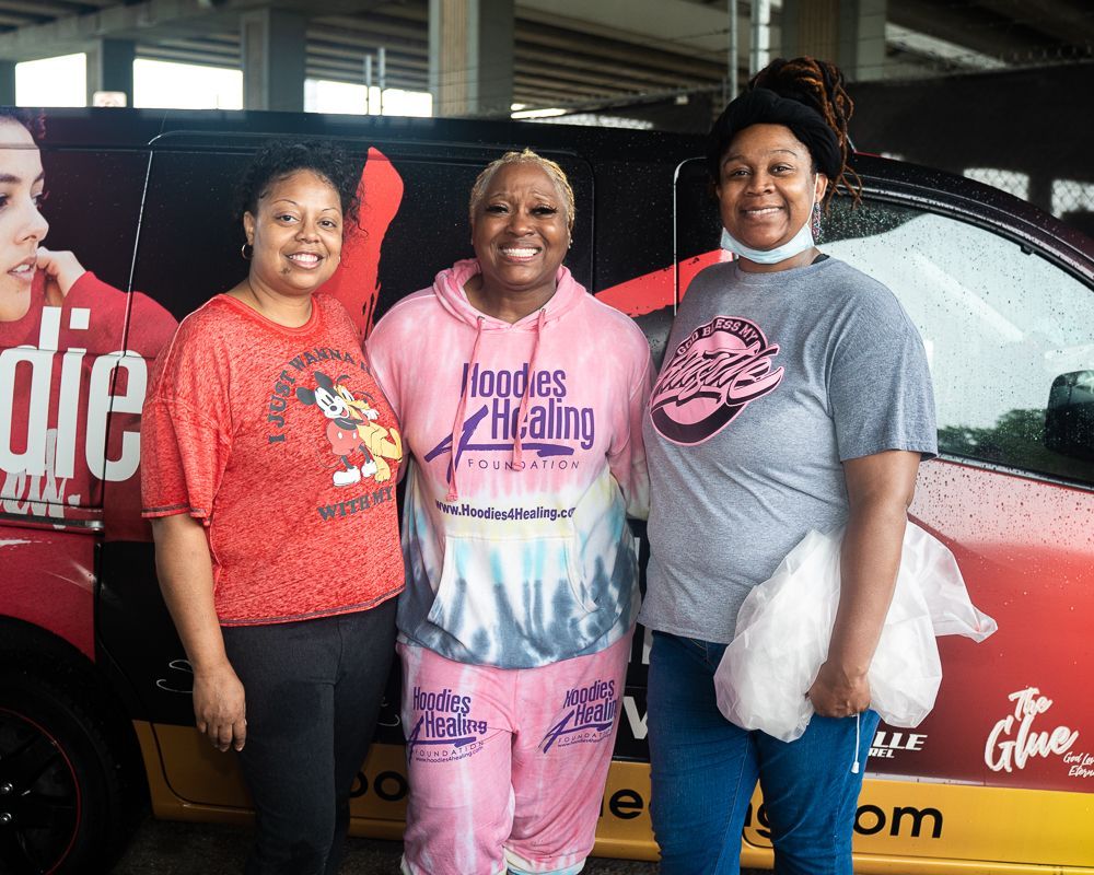 Three women are posing for a picture in front of a van that says noodles healing