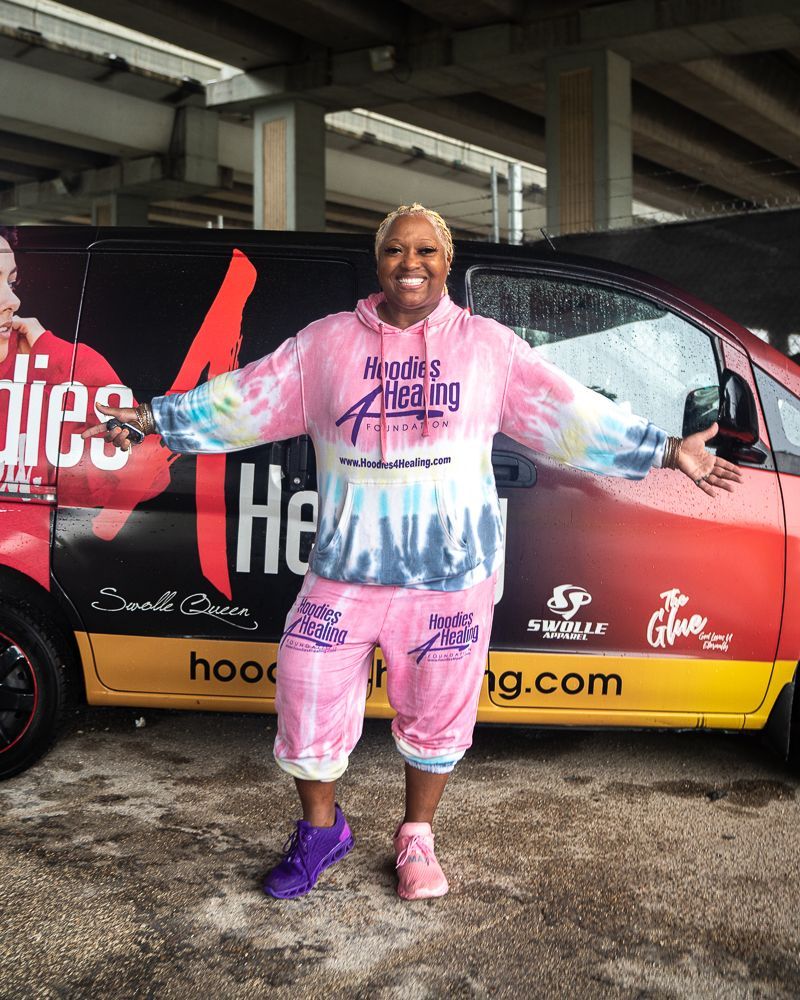 A woman in a pink tie dye hoodie is standing in front of a van.