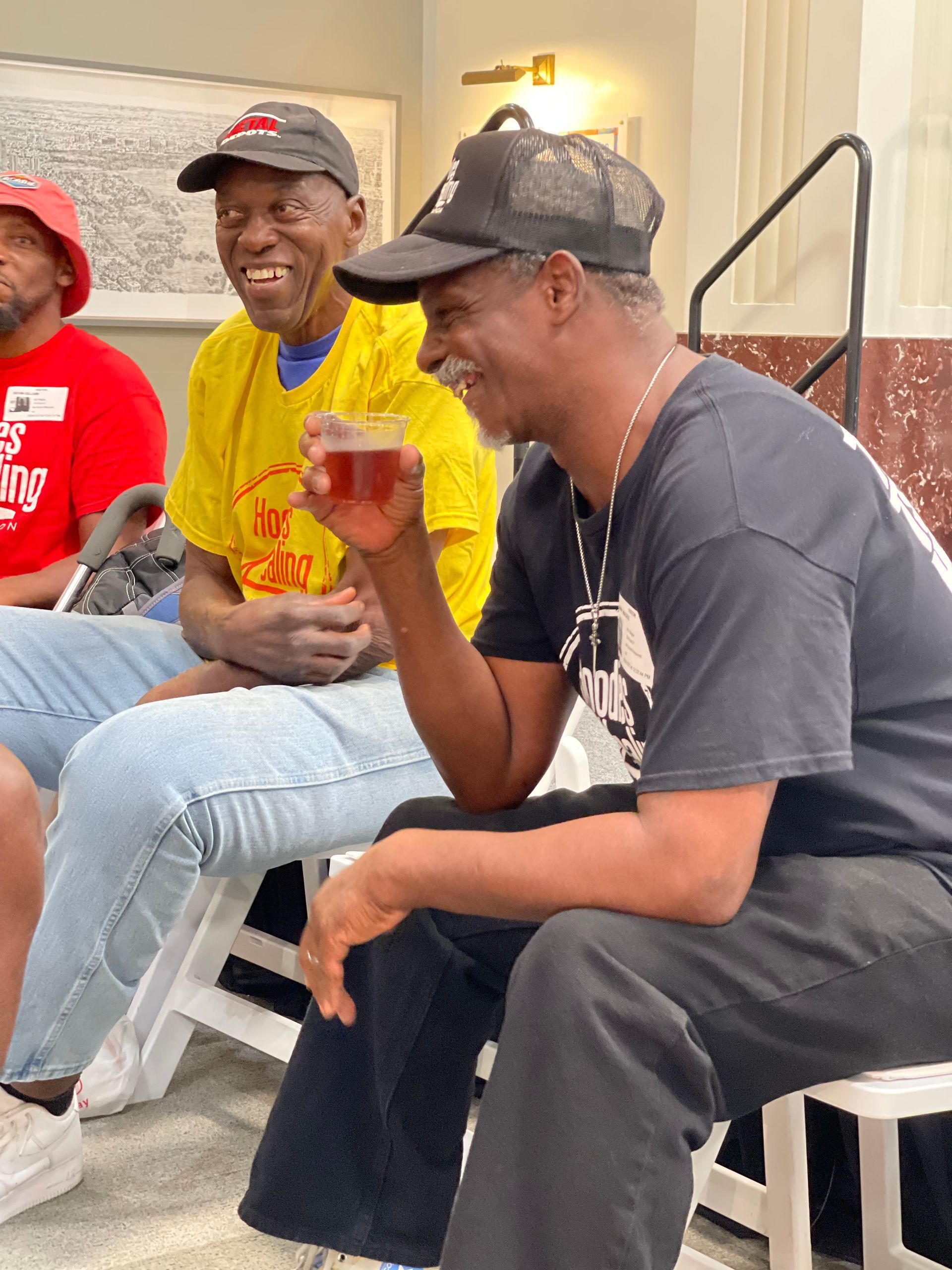 A group of men are sitting on chairs and one of them is holding a glass of beer.
