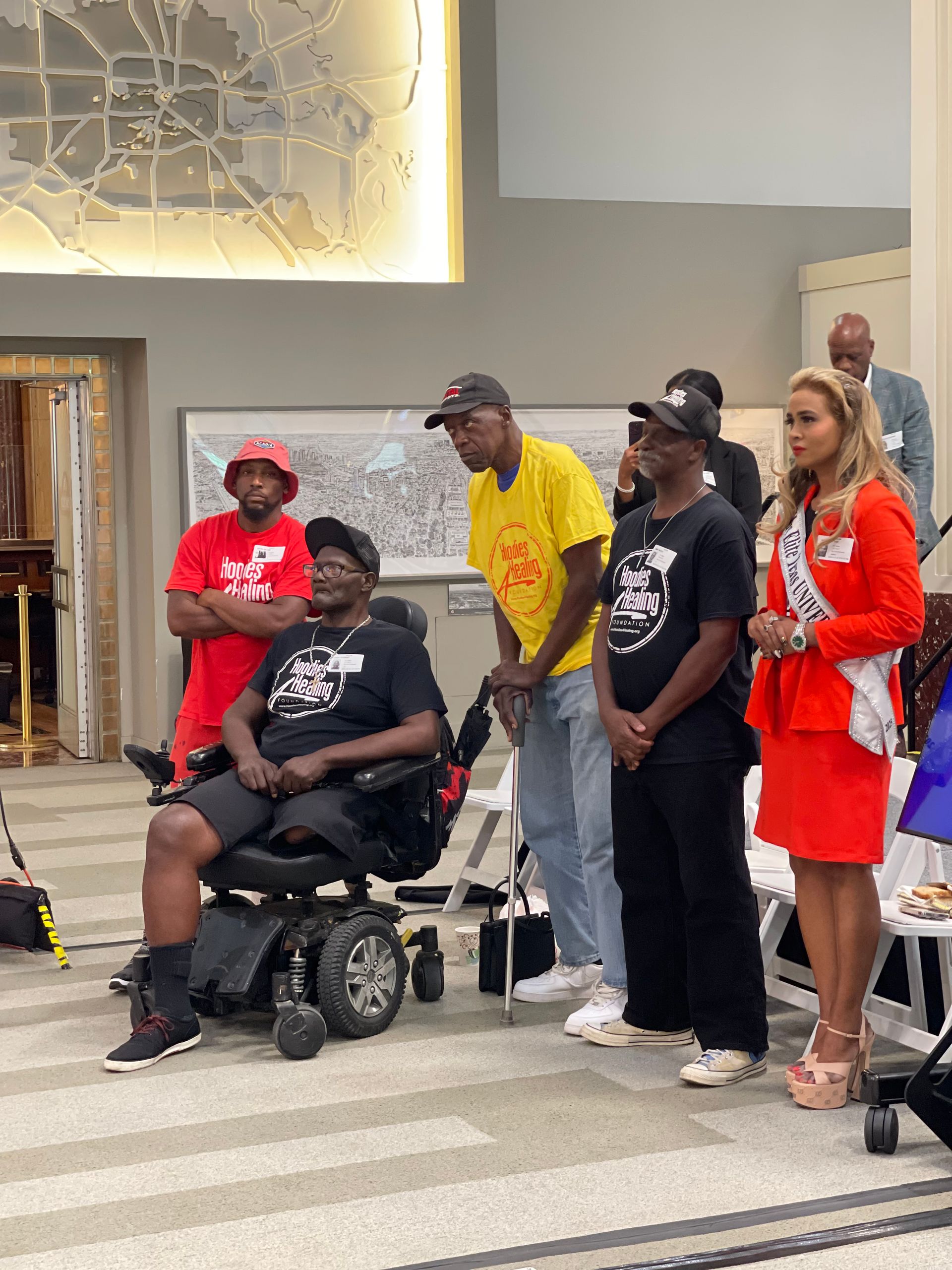 A group of people are standing around a man in a wheelchair.
