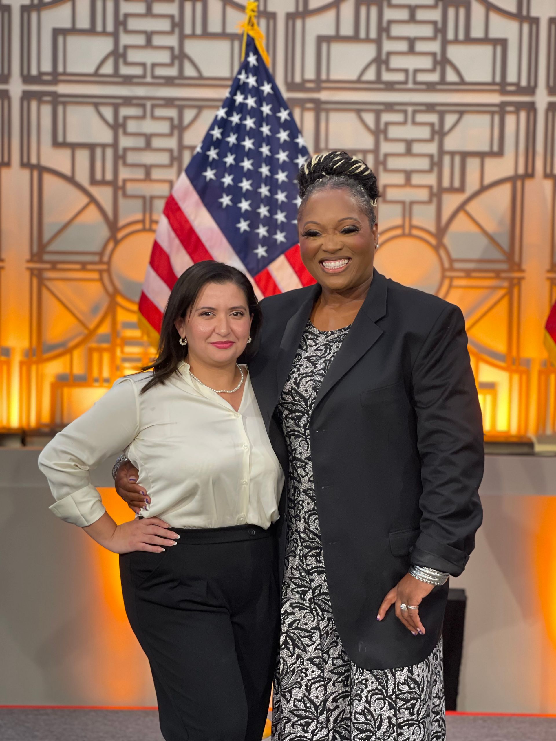 Two women pose for a picture in front of an american flag