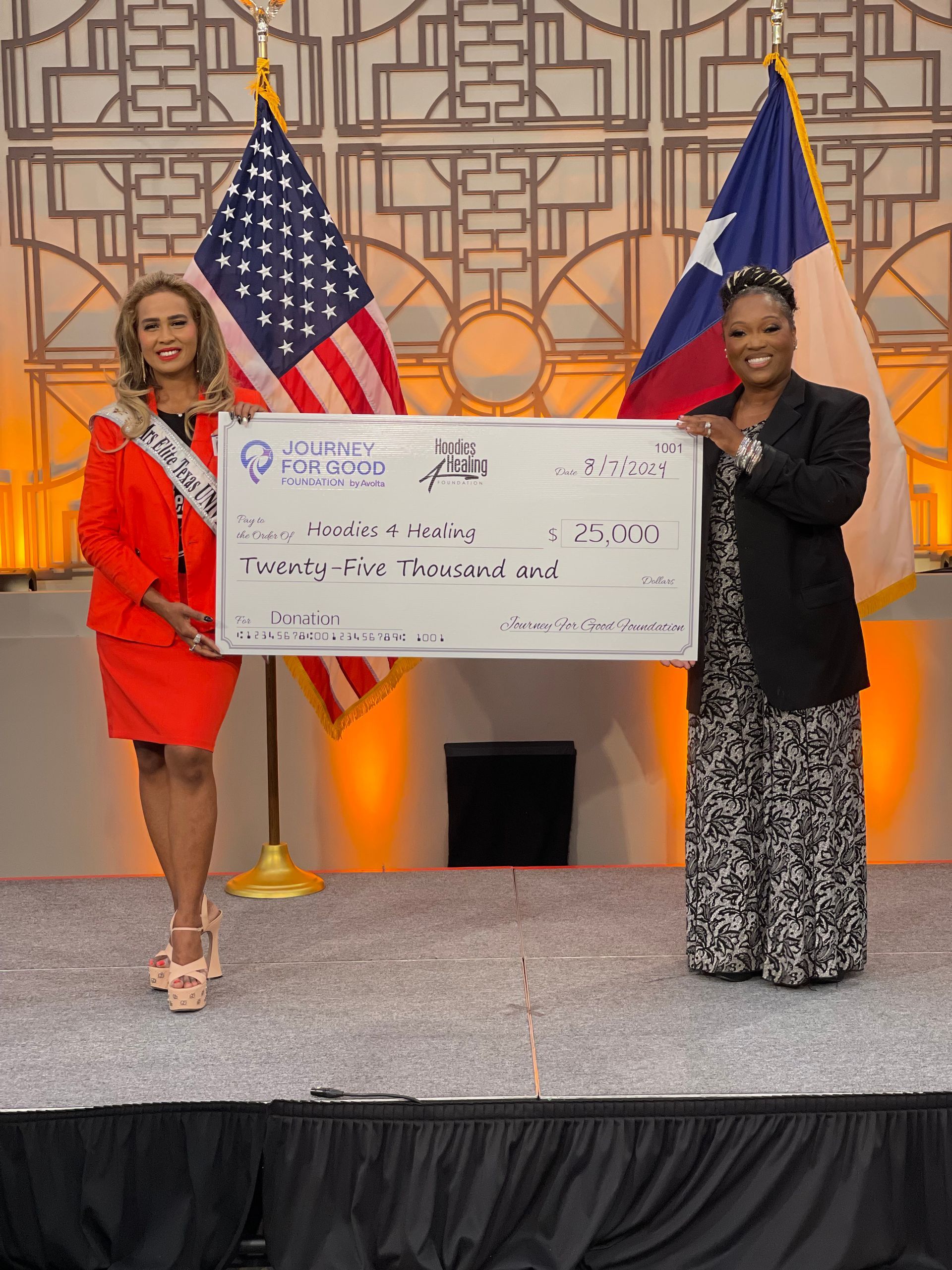Two women are standing on a stage holding a large check.