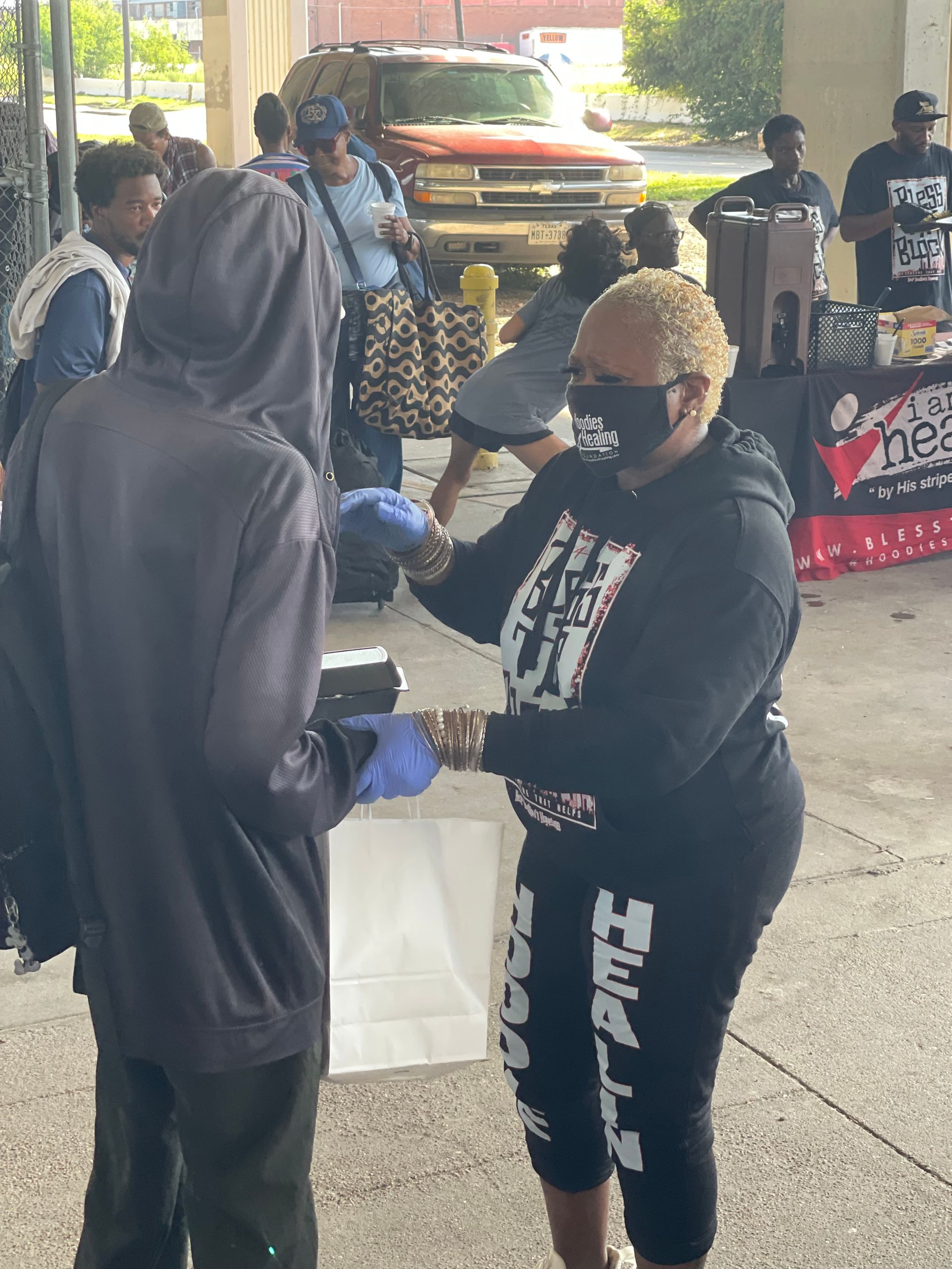 A woman wearing a mask is giving a man a bag of food.
