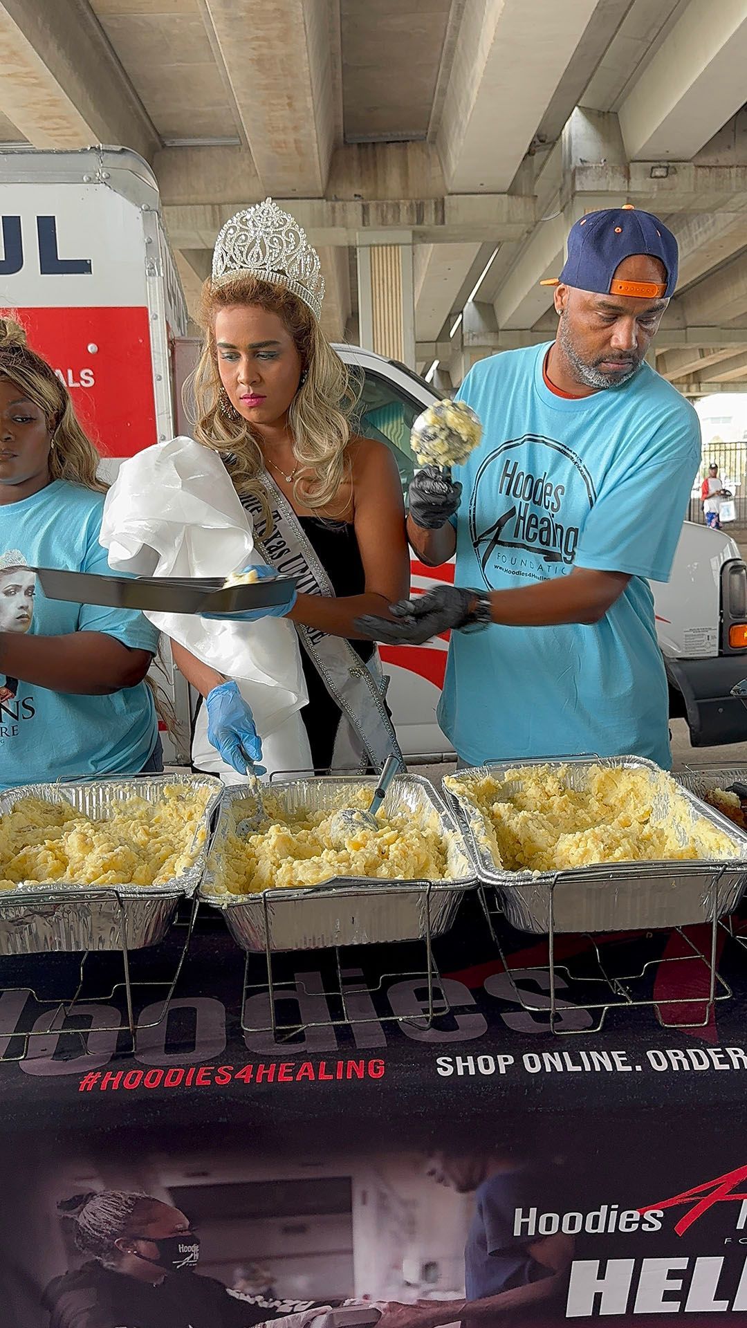 A woman in a crown is standing next to a man preparing food.