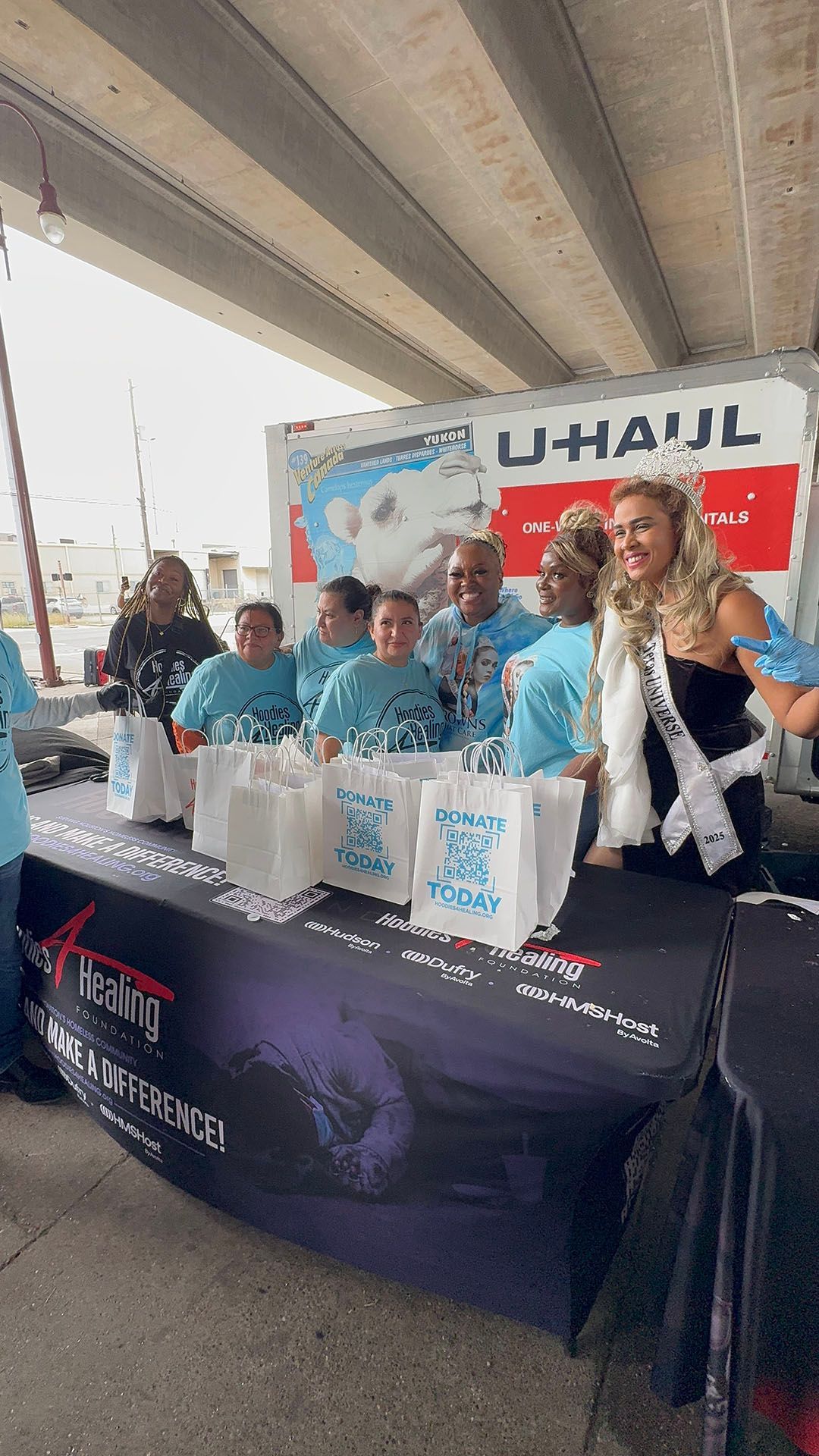 A group of people are standing around a table in front of a u-haul truck.
