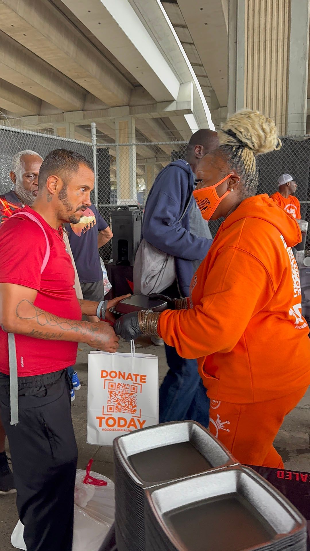 A man in a red shirt is talking to a woman in an orange hoodie.