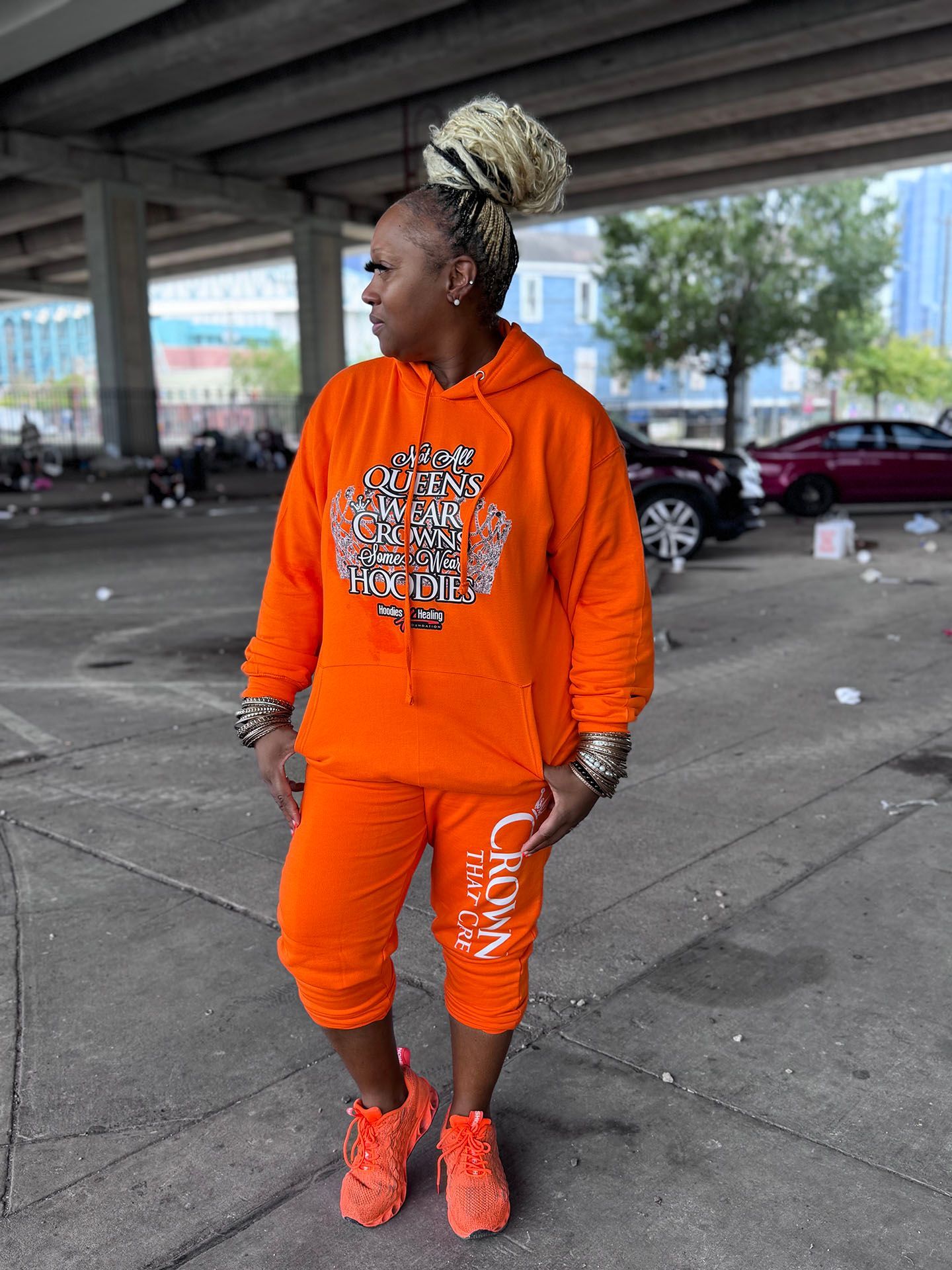 A woman wearing an orange hoodie and orange sweatpants is standing on a sidewalk.