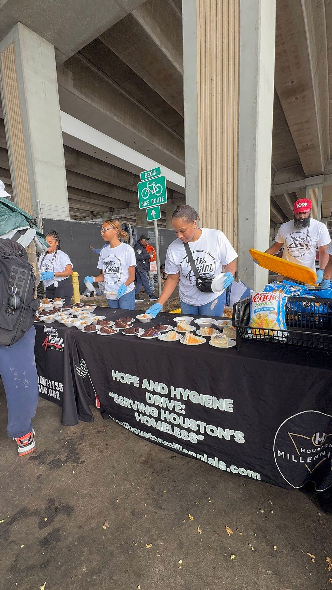 A group of people are standing around a table with food on it.
